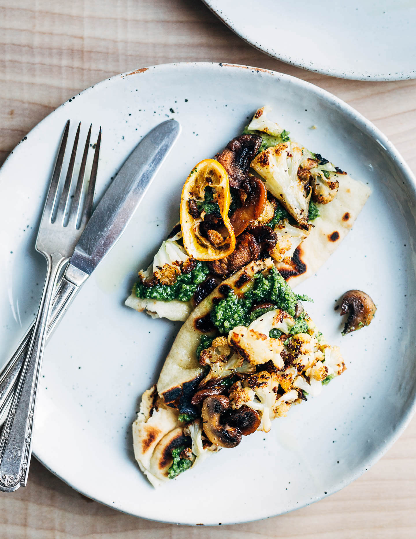 Two triangles of roasted cauliflower flatbreads arranged on a plate and drizzled with olive oil.