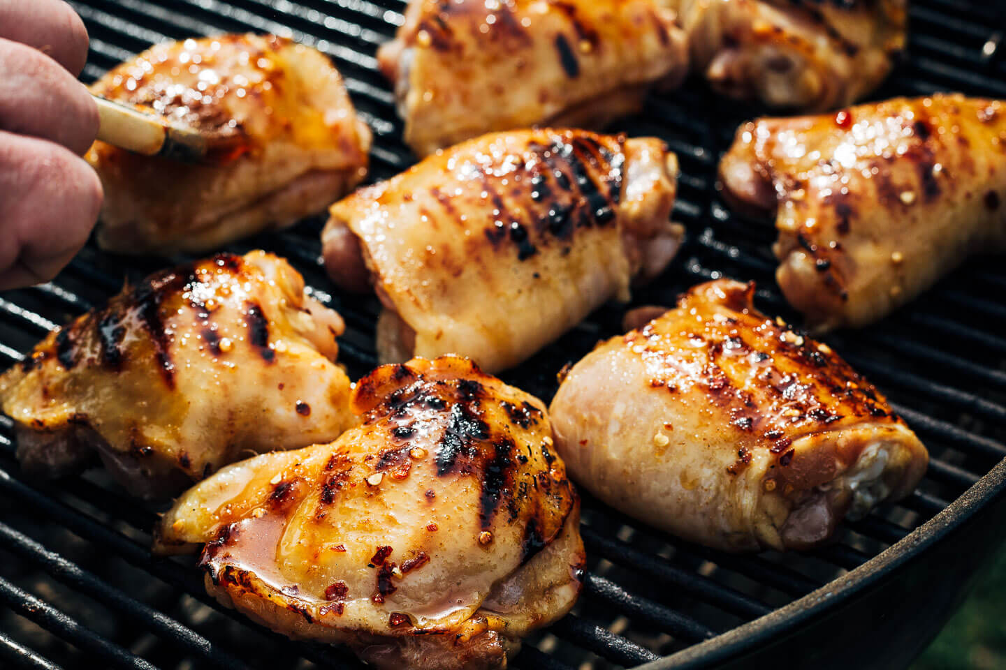 Chicken thighs on the grill, getting brushed with hot honey. 