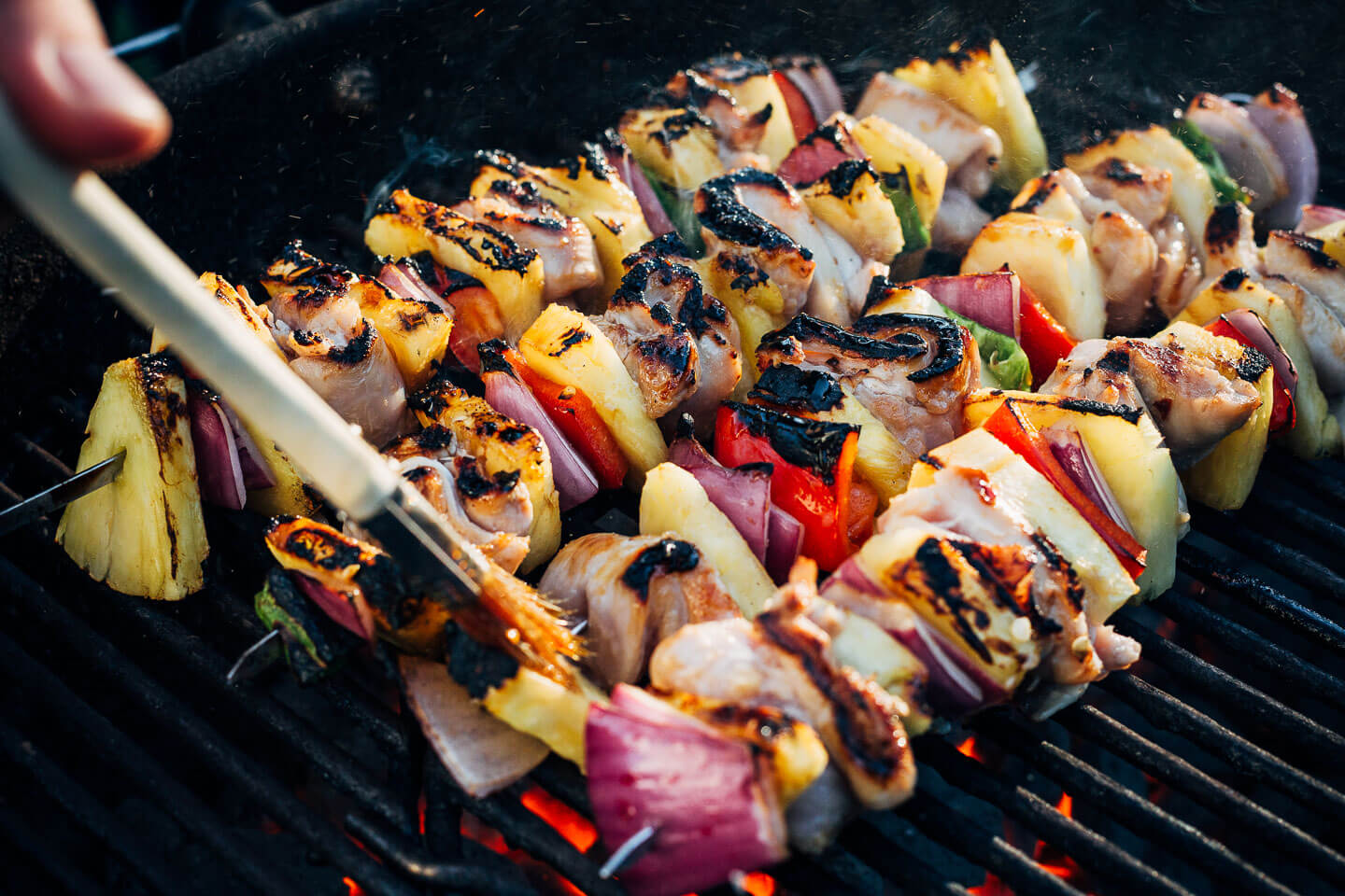 Pineapple chicken kebabs being brushed with marinade on the gill. 