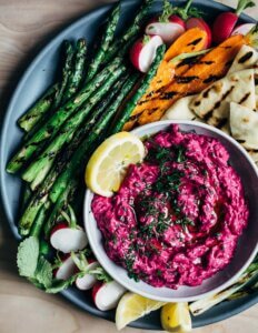 A platter of grilled vegetables with bright pink beet dip in the middle.
