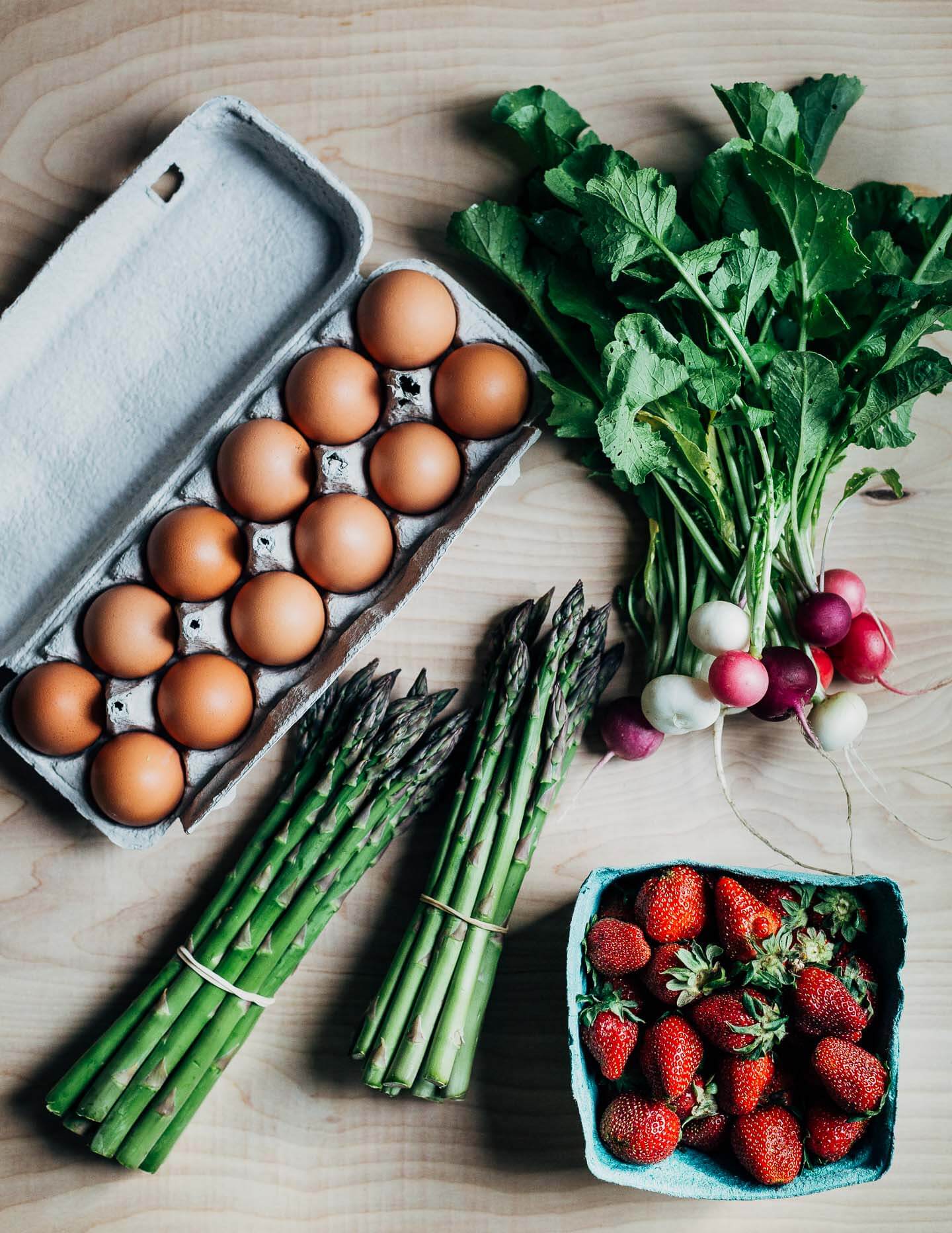 Spring produce guide, featuring eggs, radishes, two bunches asparagus, and strawberries
