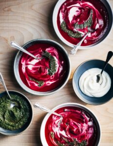 Bowls of pink soup with green pistou and little bowls of pistou and cream alongside.