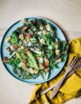 A blue platter toped with a Caesar salad and salad tongs on the side.