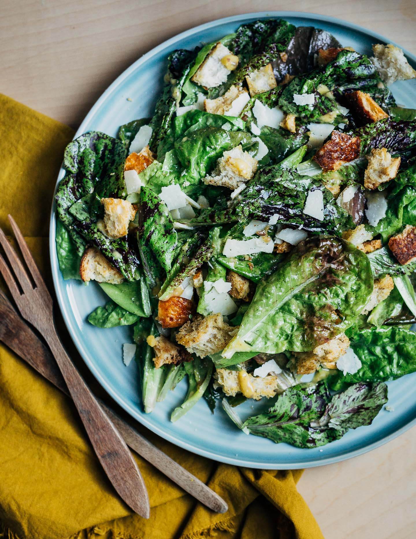 A blue platter toped with a Caesar salad and salad tongs on the side.