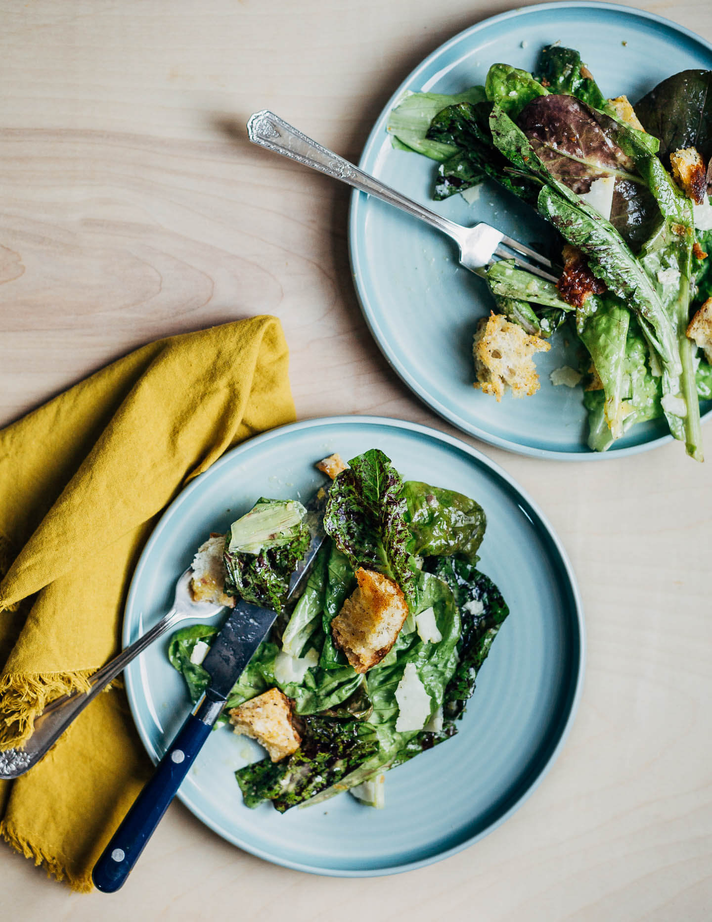 Two plates with Caesar salad and forks and knives. 