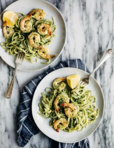 Two bowls of pesto pasta topped with shrimp.