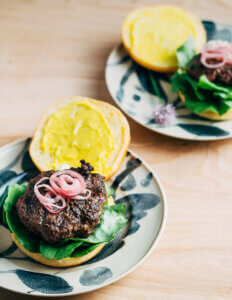 Two plates with burgers. Burgers are layered with shallots and lettuce.