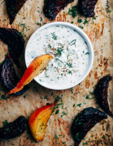 A bowl of tzatziki on a baking sheet with roasted beet wedges.