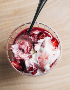 A glass filled with strawberries in syrup and vanilla ice cream