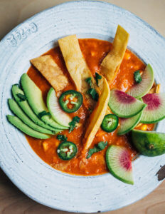 A bowl of tortilla soup with tortilla strips, sliced radishes, and sliced avocados