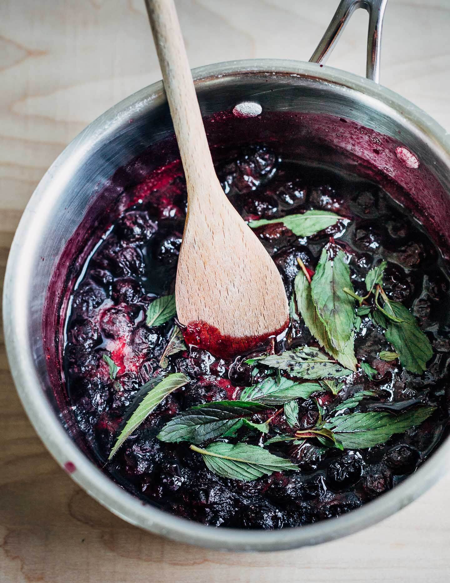 A saucepan with blueberry sauce and mint. 