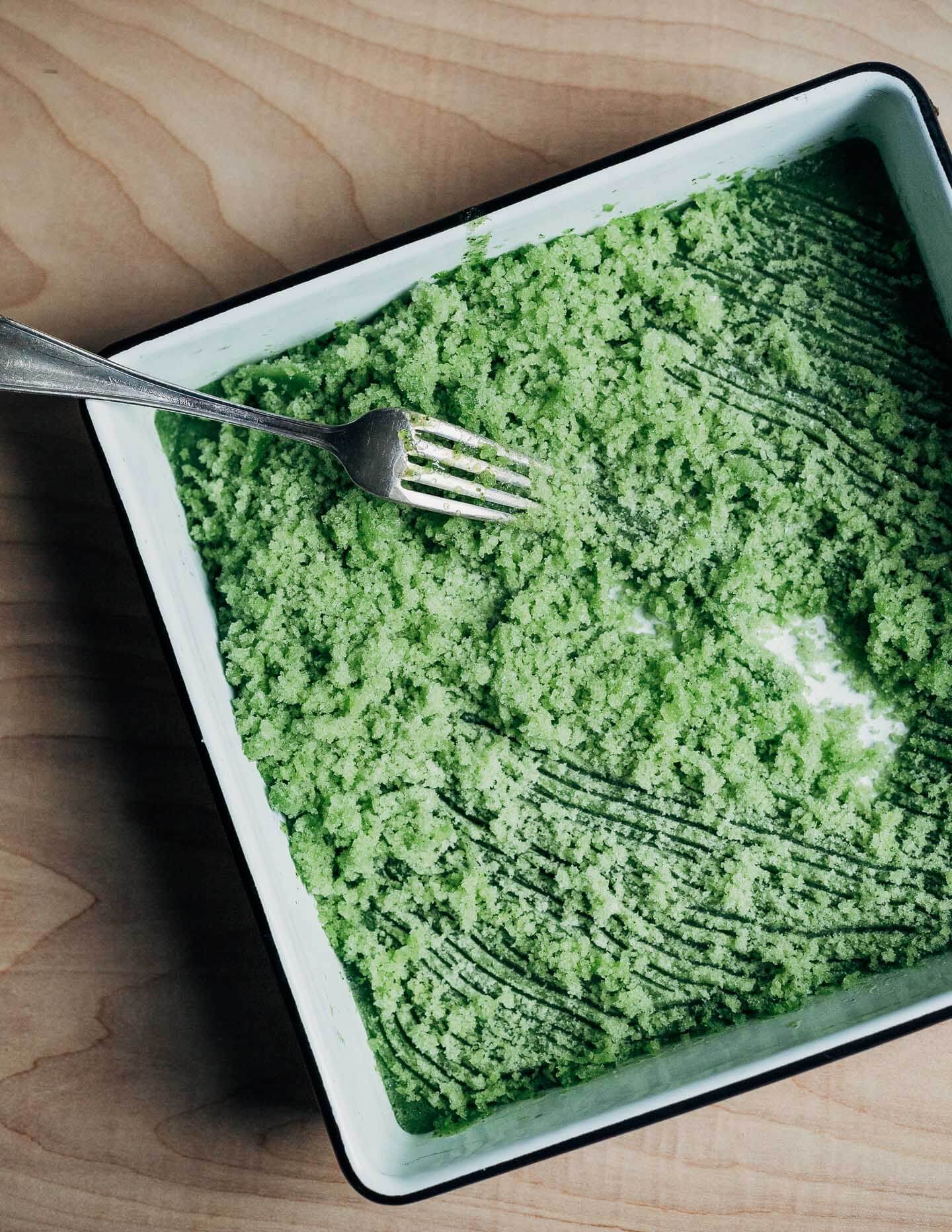 An enamel pan filled with granita being scraped by a fork.