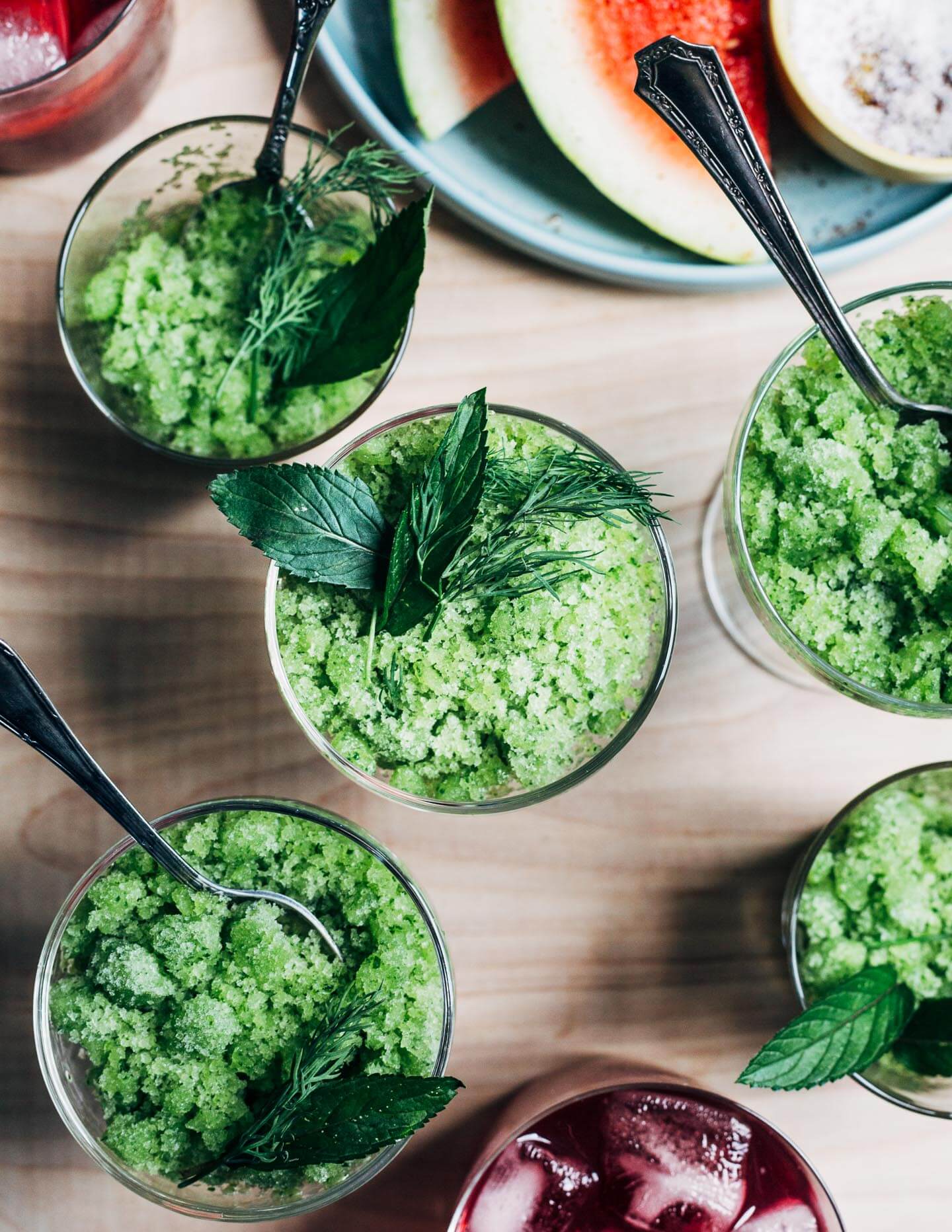 Small glasses filled with cucumber granita and garnished with herbs.