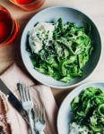 Two bowls of bright green pasta noodles with drinks and utensils on the side.