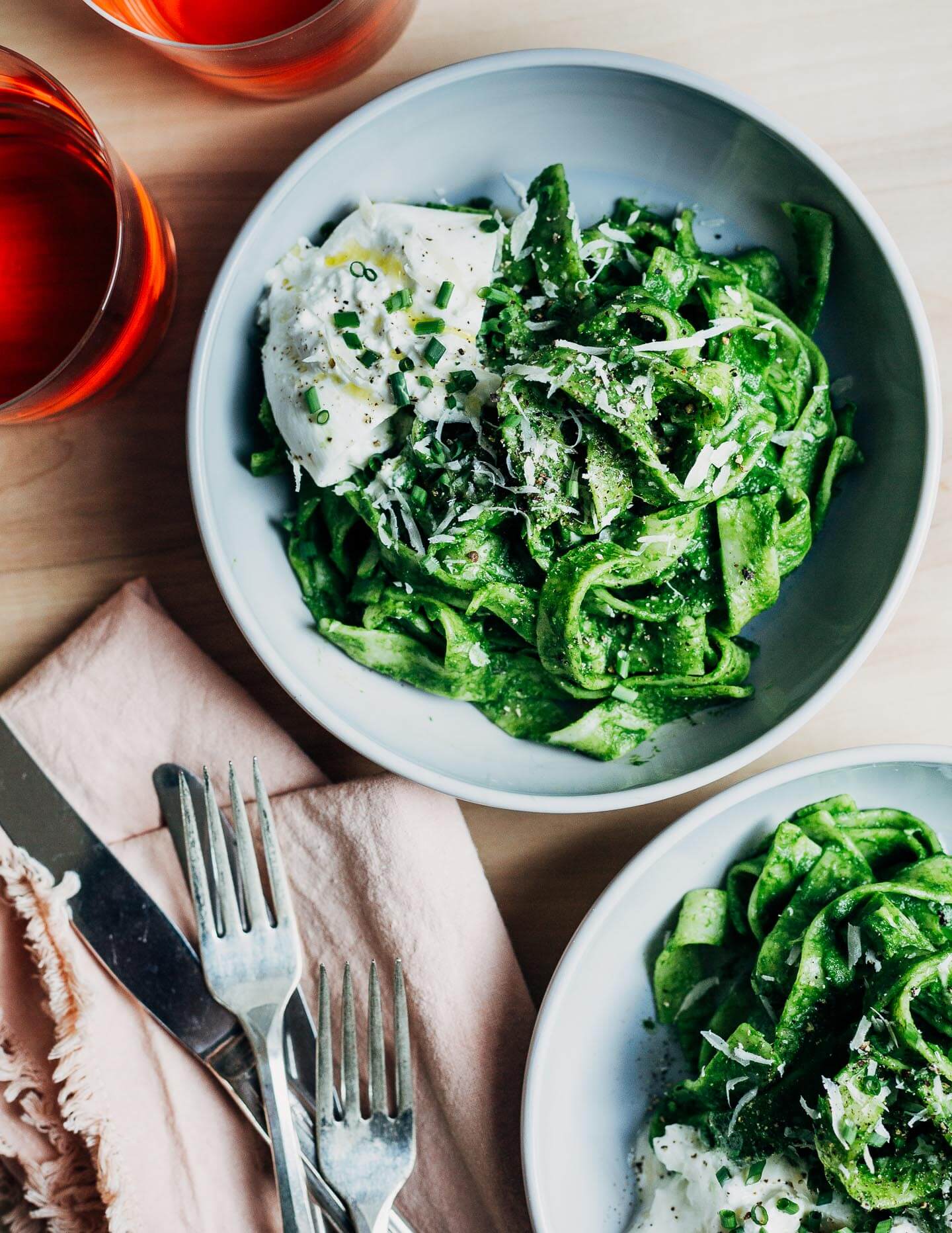 Two bright green pasta noodles with drinks and utensils on the side. 