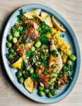 A platter with roasted chicken, couscous, olive, lemons, and herbs.