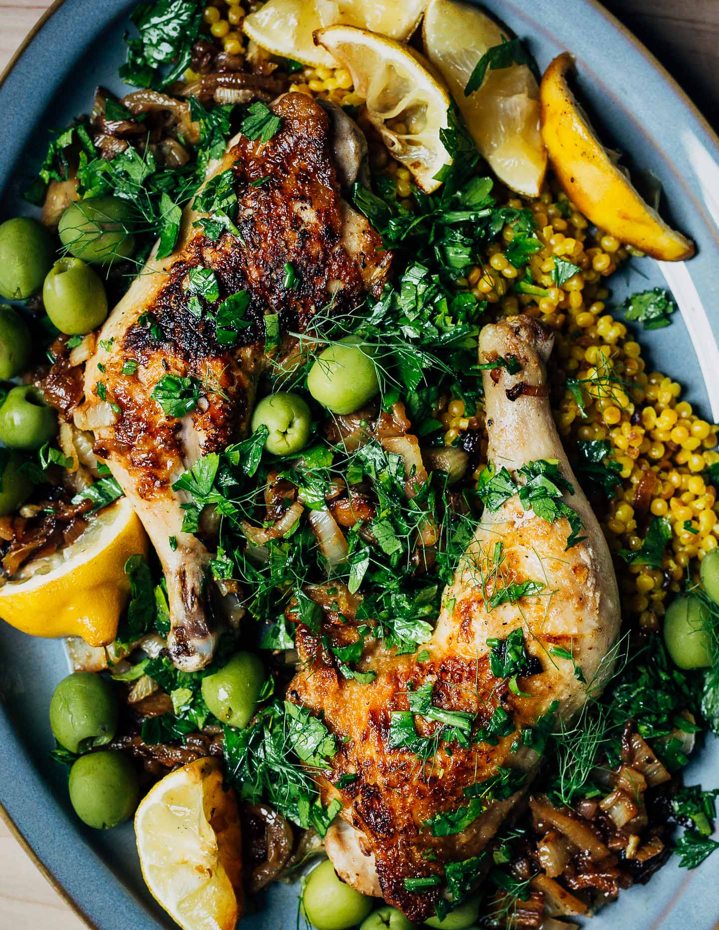A platter with roasted chicken, couscous, olive, lemons, and herbs.