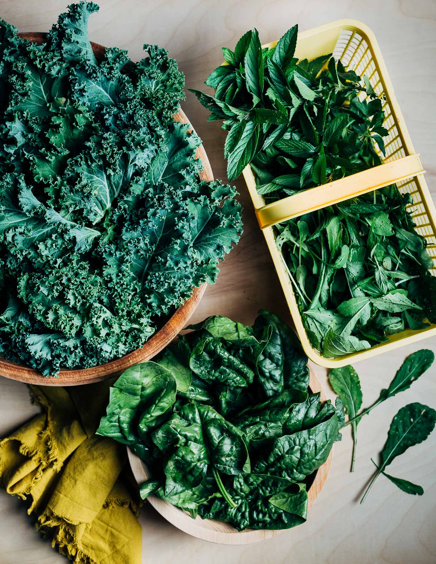 Bowls and small baskets filled with kale, spinach, and herbs. 