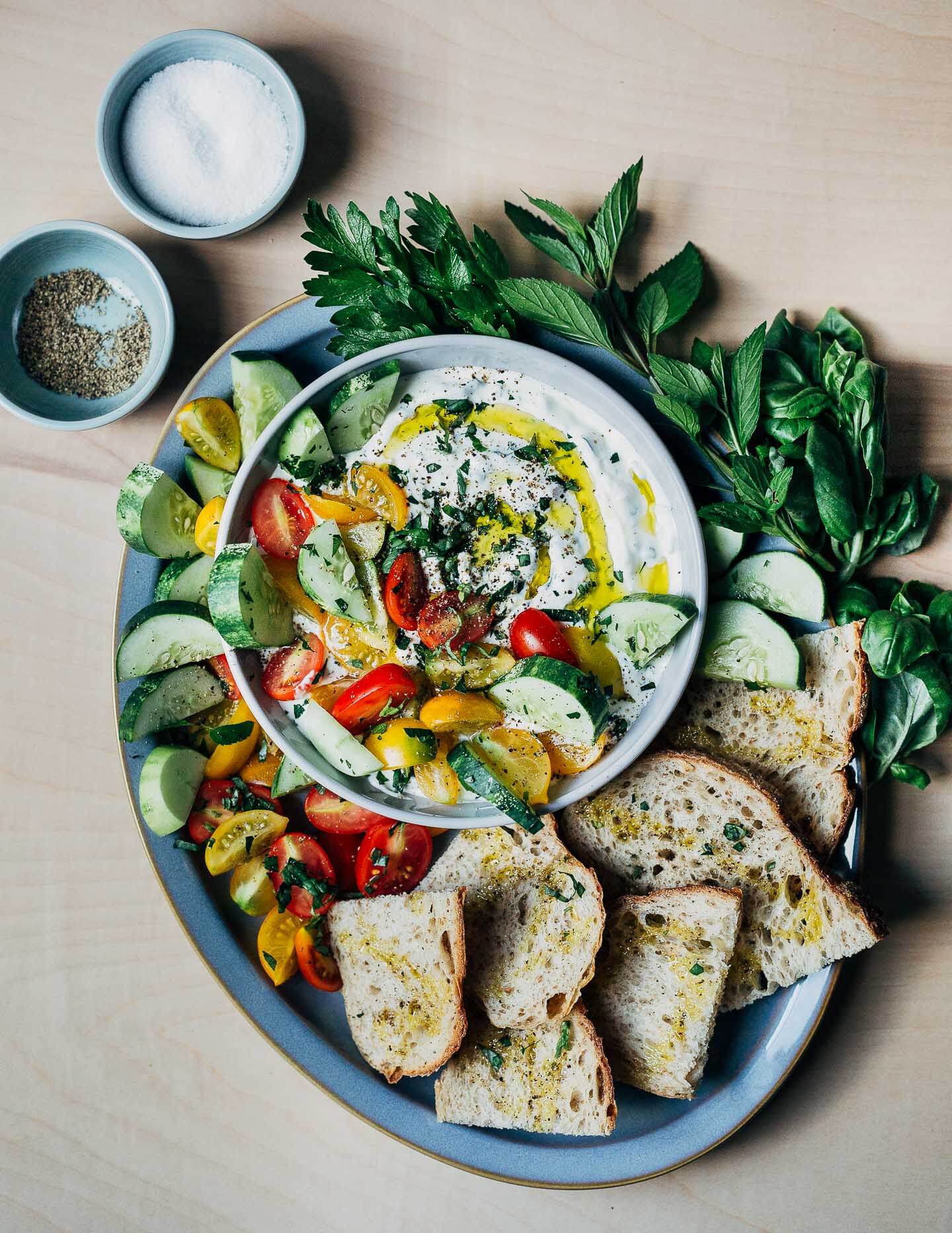 A platter with toasts and vegetables and a bowl of dip with sea salt and pepper. 