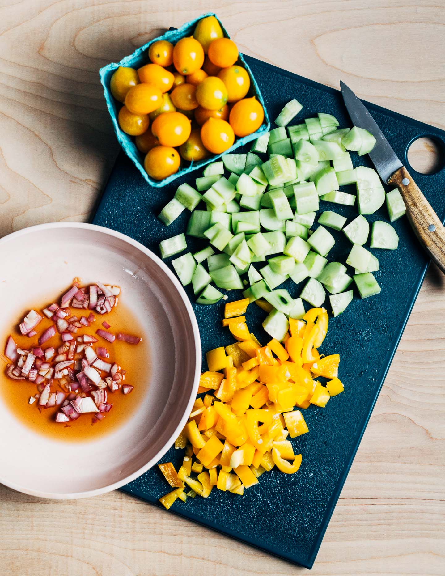 A cutting board with yellow cherry tomaotes and cut up vegetables. 