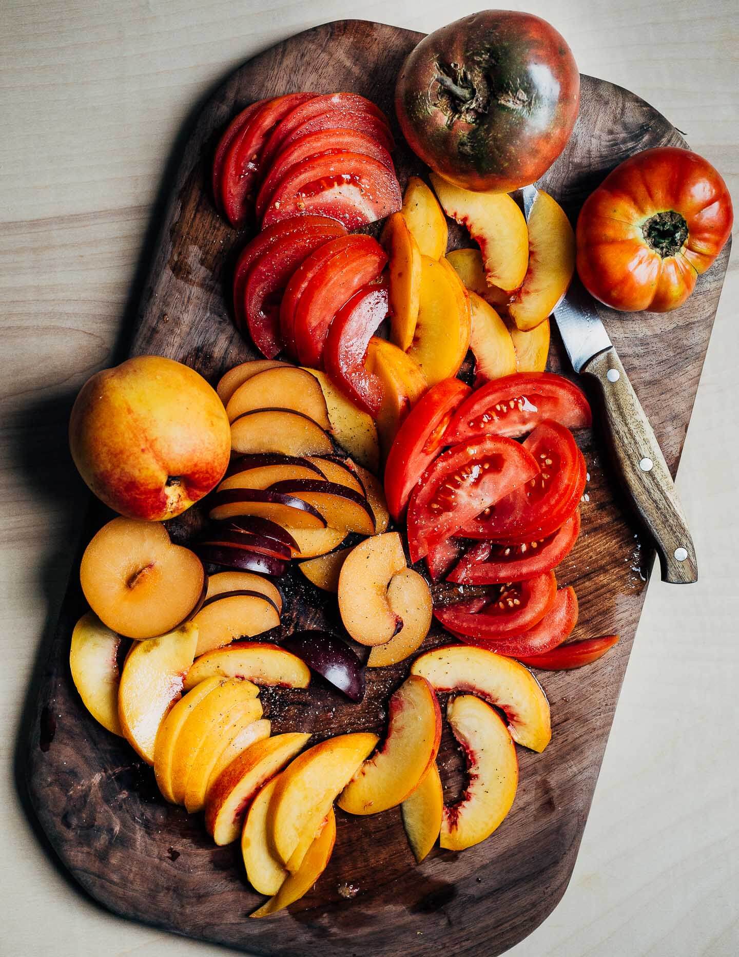 A cutting board with sliced fruit and tomatoes. 