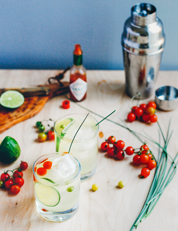 A table with two cocktails, cherry tomatoes and a cocktail shaker. 