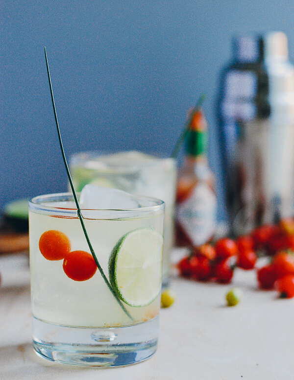 A table with two cocktails, cherry tomatoes and a cocktail shaker. 