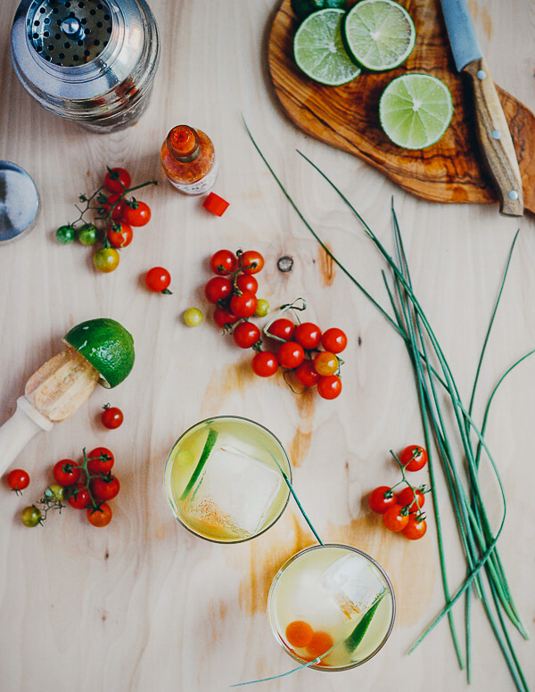 A table with two cocktails, cherry tomatoes and a cocktail shaker. 