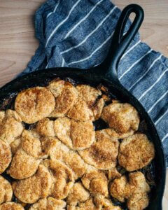 A skillet with apple pandowdy. It has a layered, golden pastry crust.