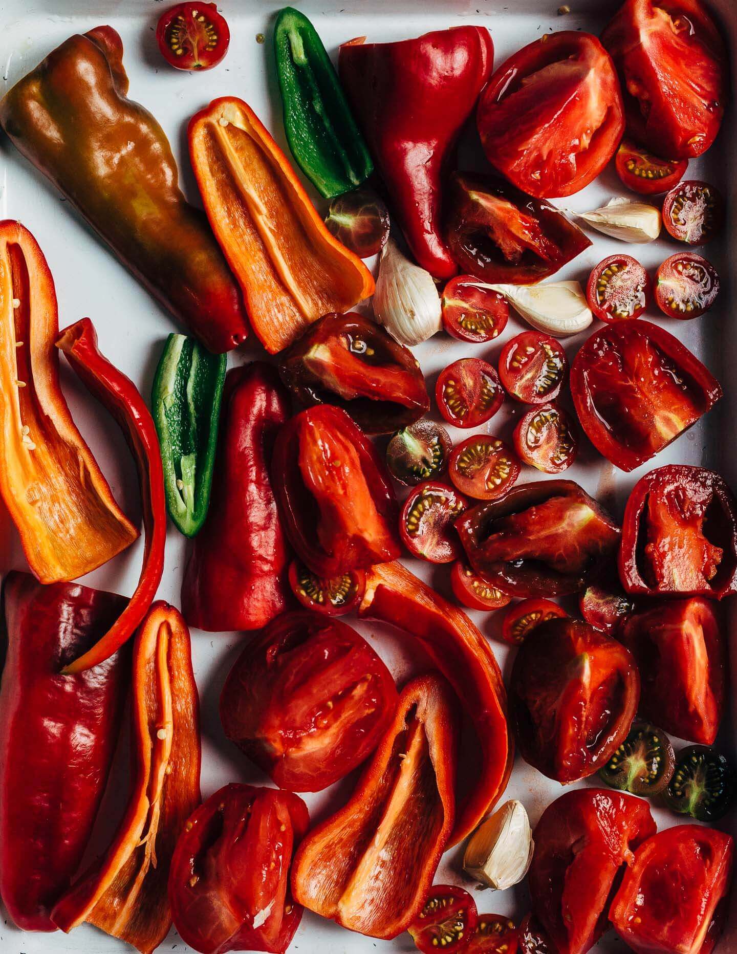 A tray with cut up peppers and tomatoes, ready to roast. 