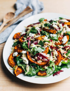 A platter of salad with roasted butternut squash, leafy greens, and orzo.