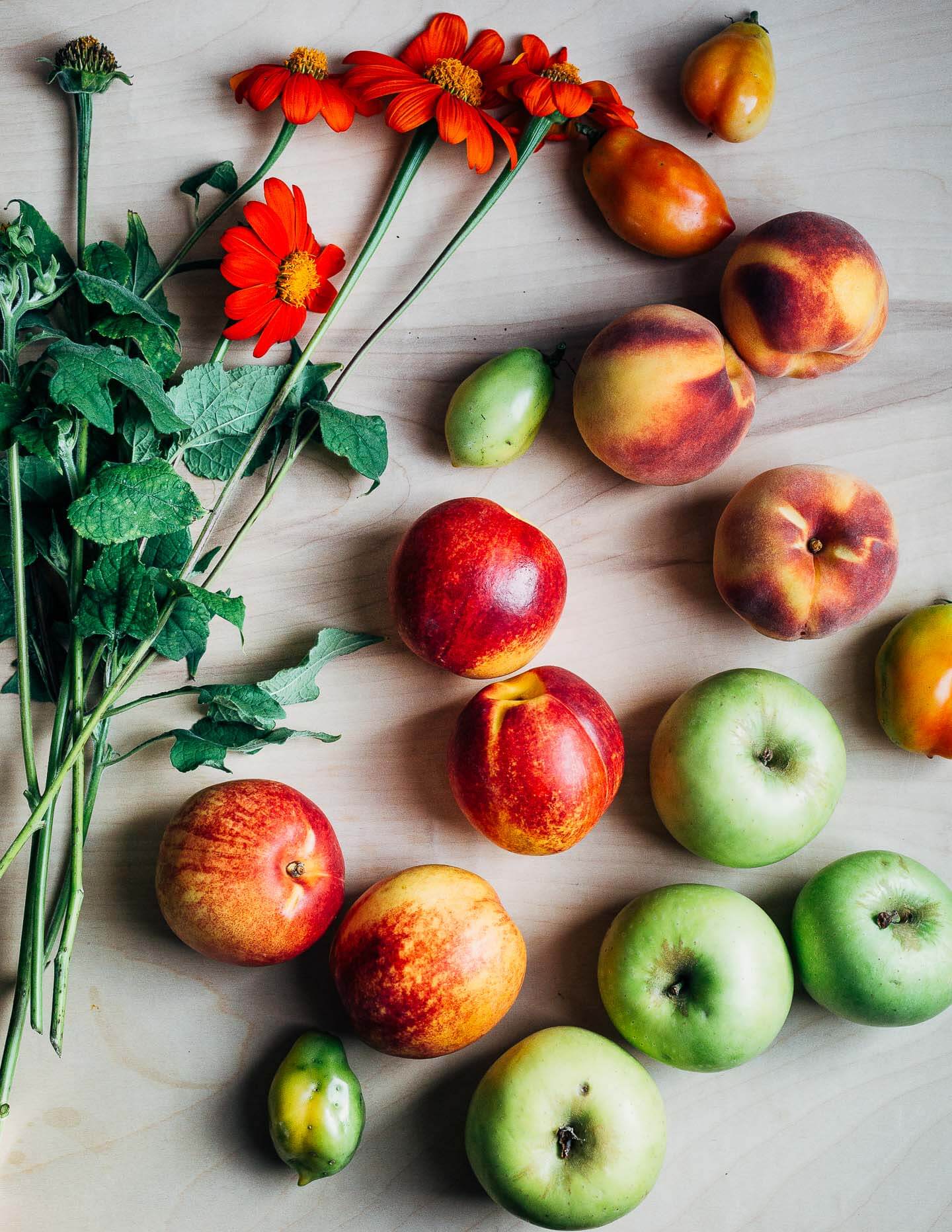 A table with orange sunflowers, nectarines, peaches, and apples. 