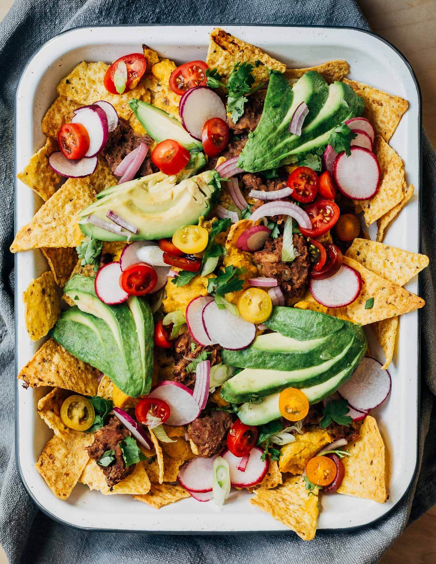 Nachos in a baking dish topped with avocados and herbs.