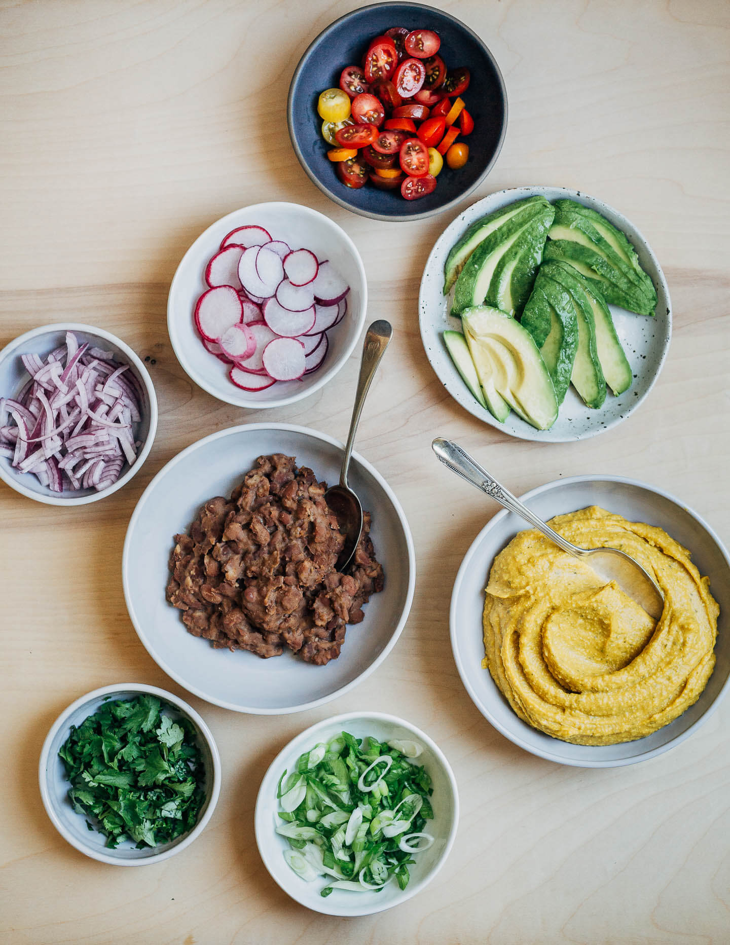 Various nacho toppings in little bowls on a table. 