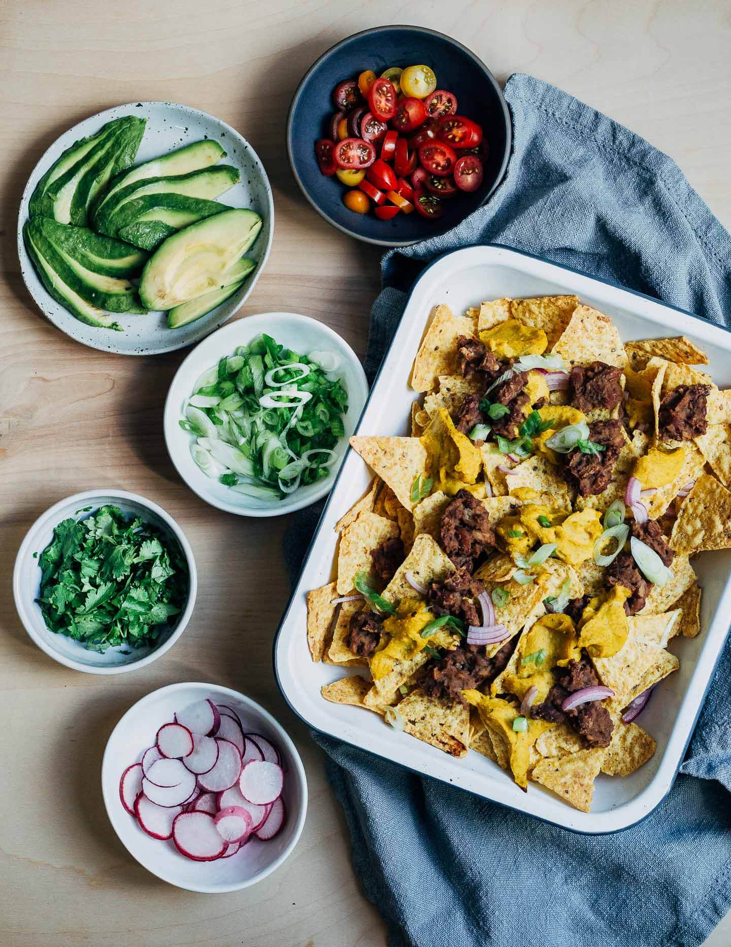 A dish of nachos next to an array of toppings. 