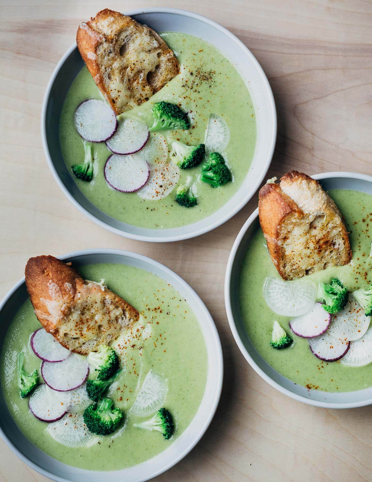 Bowls of broccoli cheddar soup with croutons and sliced radish toppings. 