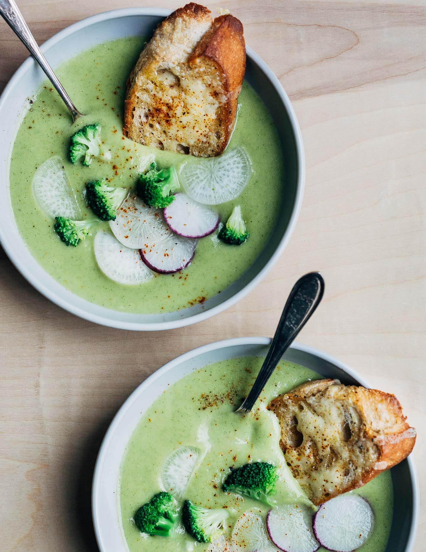 Two bowls of broccoli cheddar soup with croutons and sliced radish toppings. 