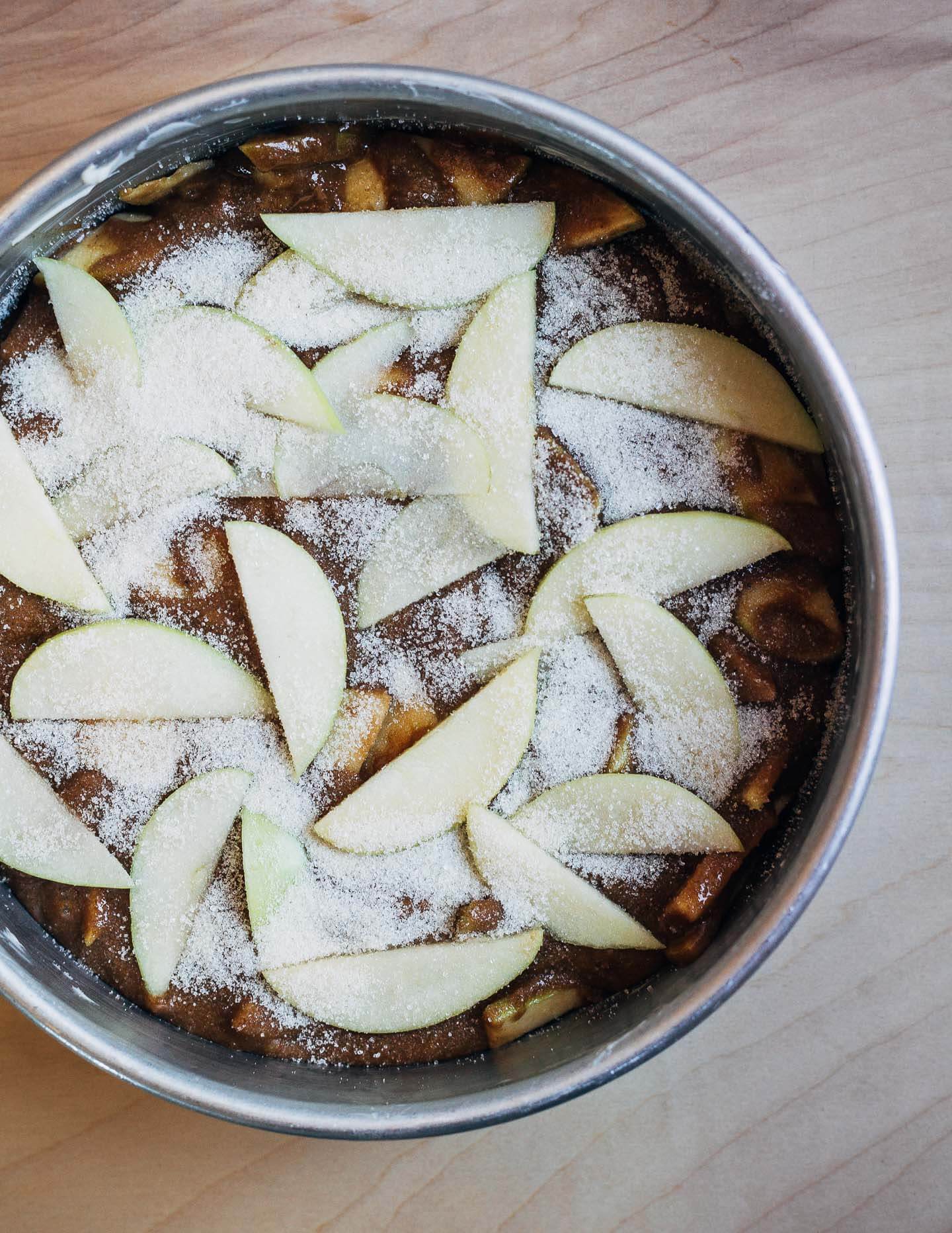 Batter in a cake pan with apples and sugar on top.