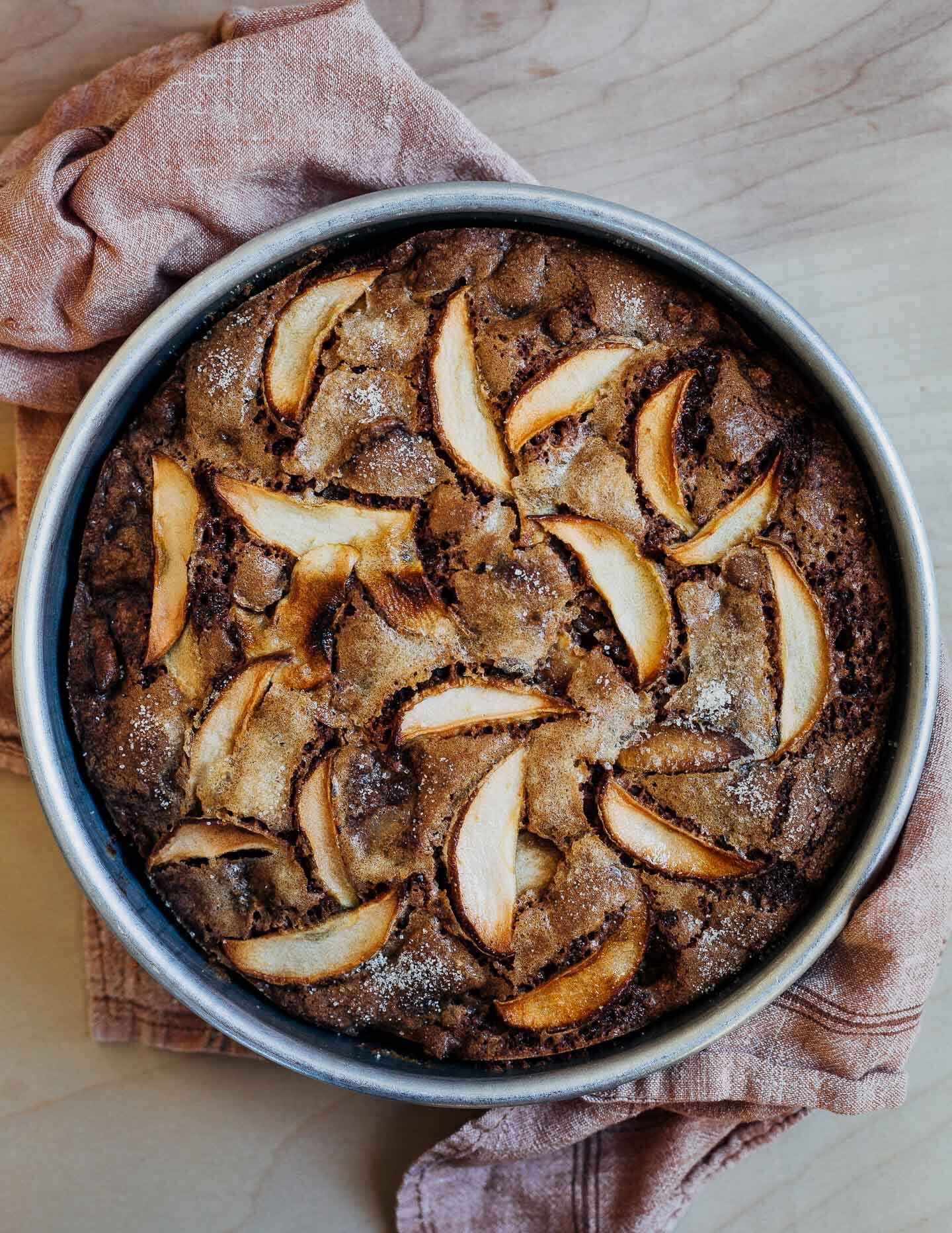 A cake pan with apple cake snd a cloth underneath. 