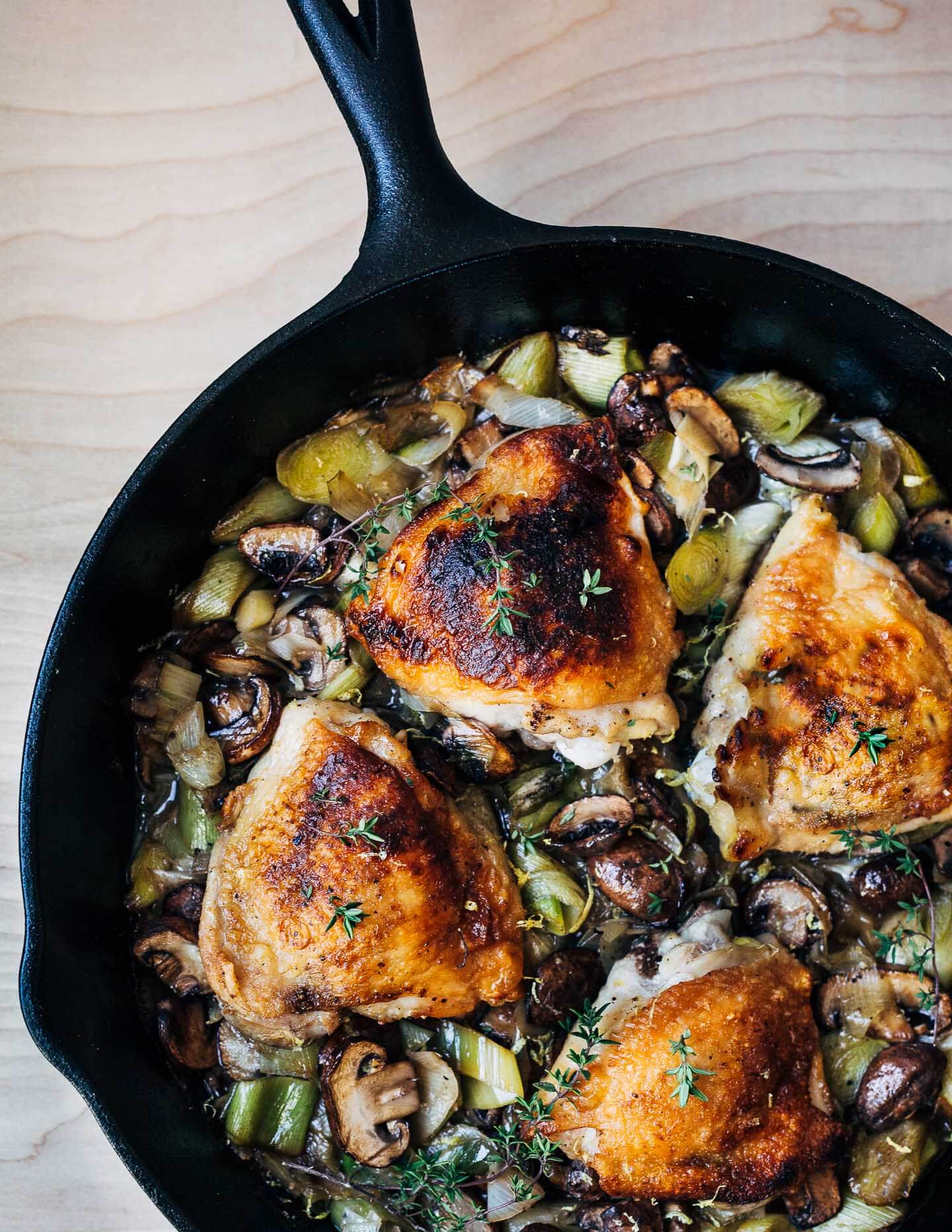 A skillet with golden chicken thighs and vegetables. 