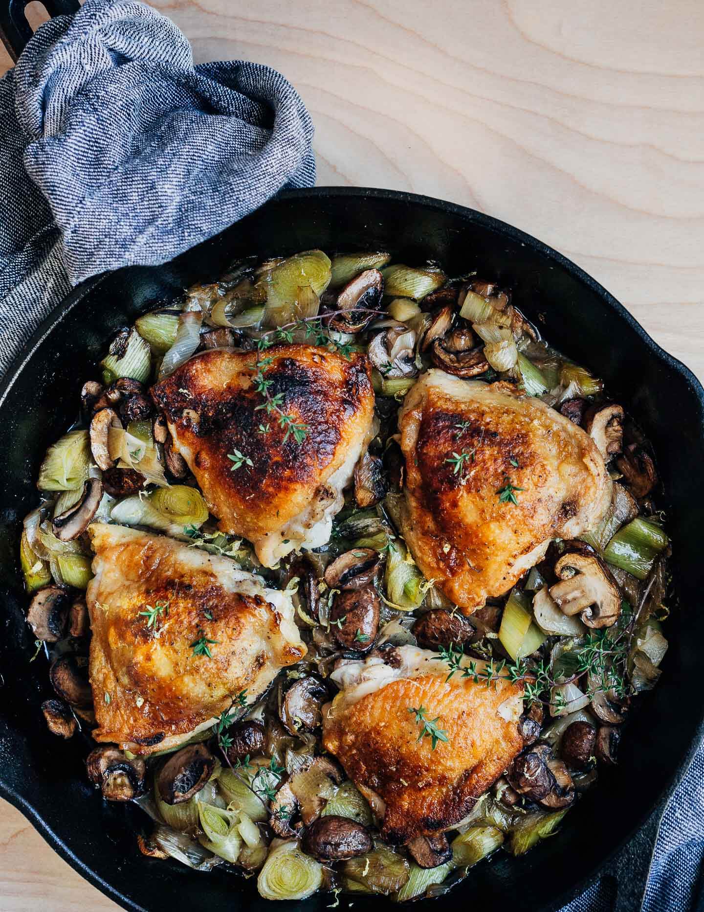 A skillet with golden chicken thighs and vegetables. 