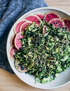 A big bowl with a kale and Brussels sprout salad topped with black and white sesame seeds.