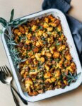 A baking dish with cornbread stuffing with serving utensils.