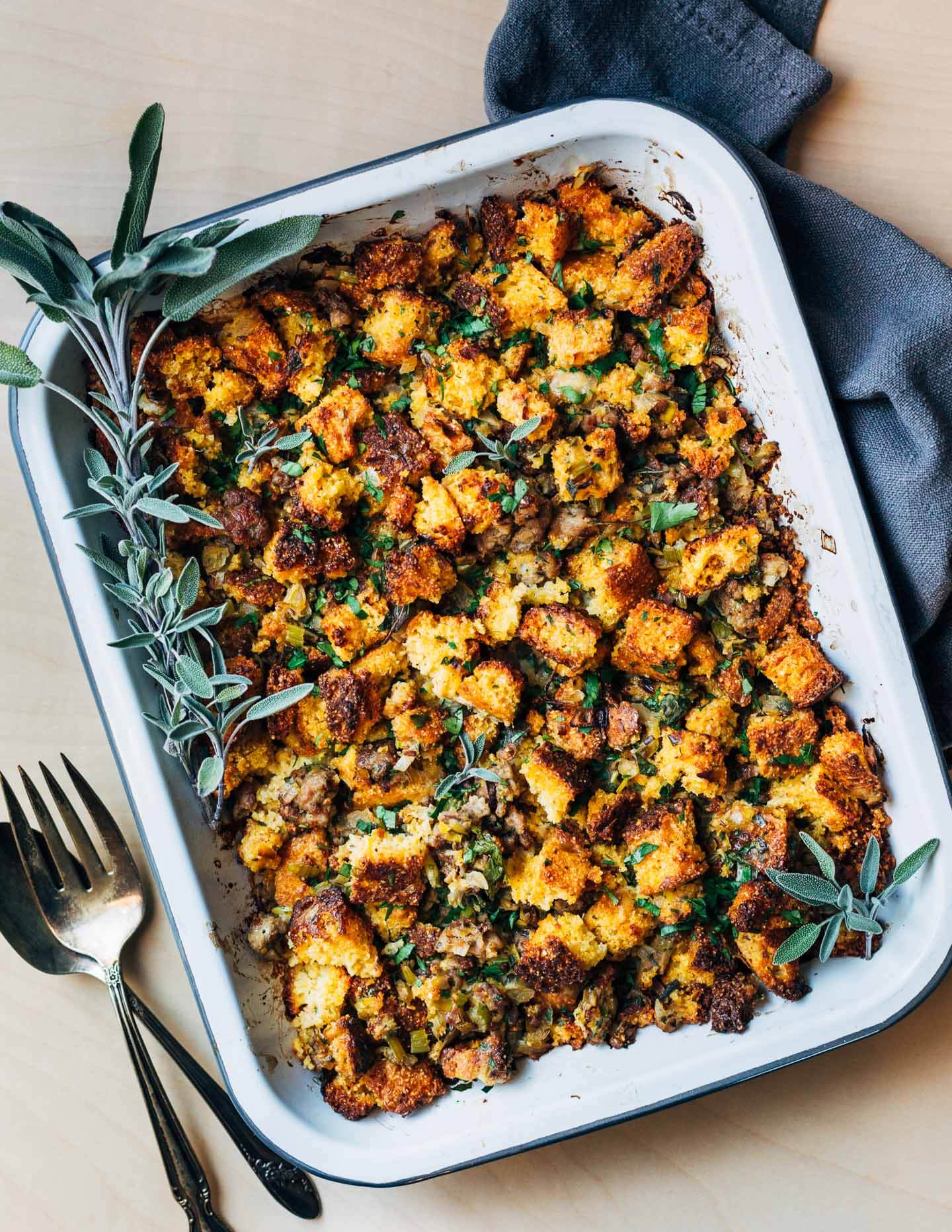 A baking dish with cornbread stuffing with serving utensils. 