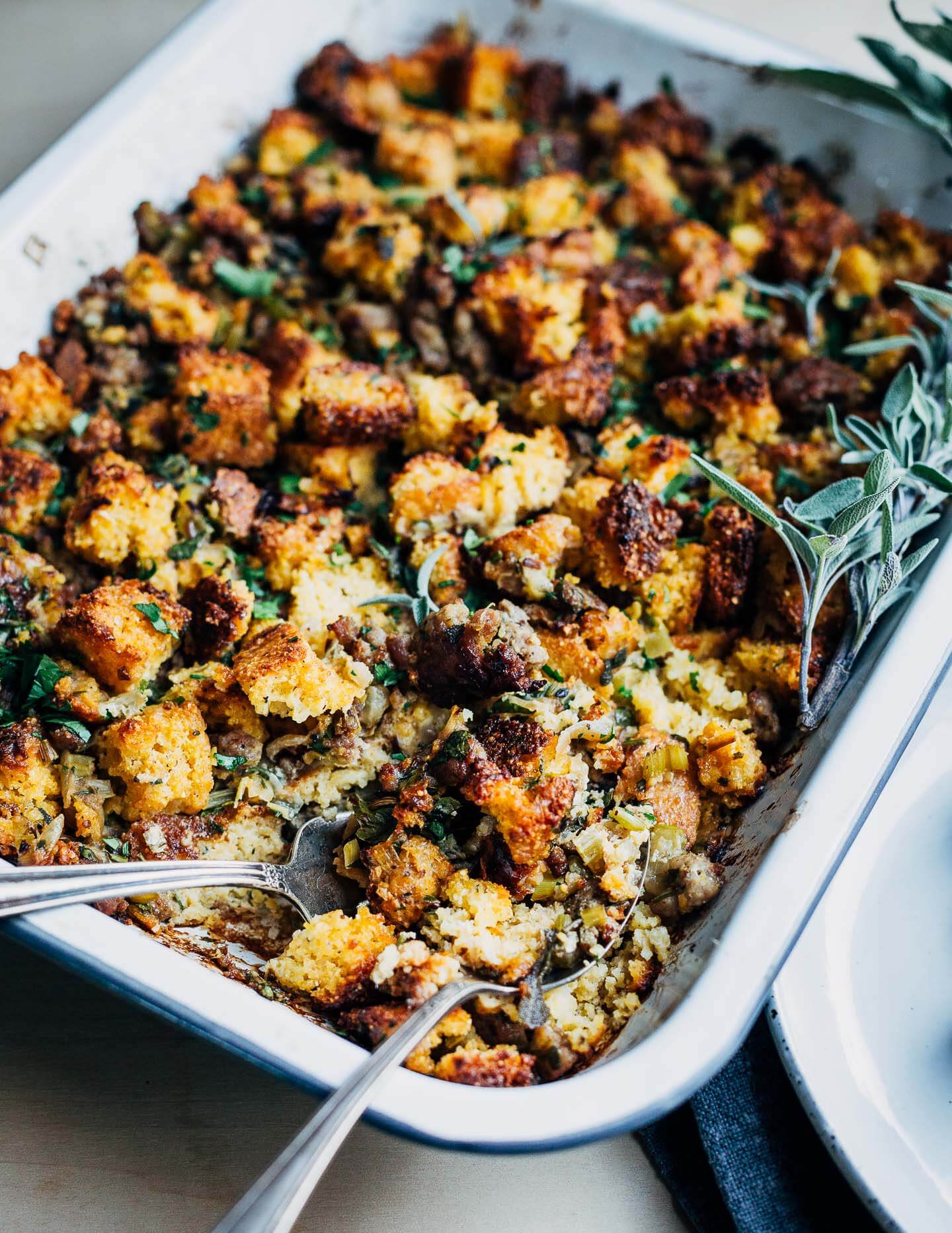 A baking dish with cooked stuffing and serving utensils. 