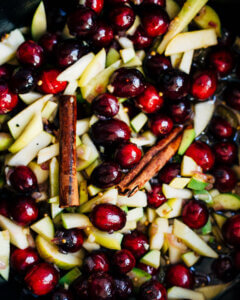 A close up view of fresh cranberries, apples, and cinnamon sticks