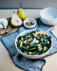 A bowl with kale, pears, and crumbled goat cheese on a table top.