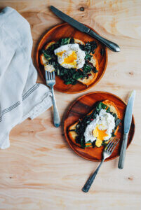 Two plates with poached eggs with greens on toast.