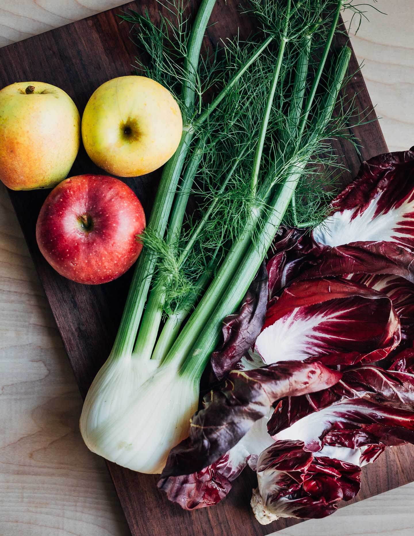 A cutting board with a fennel bulb, apples, and radicchio leaves