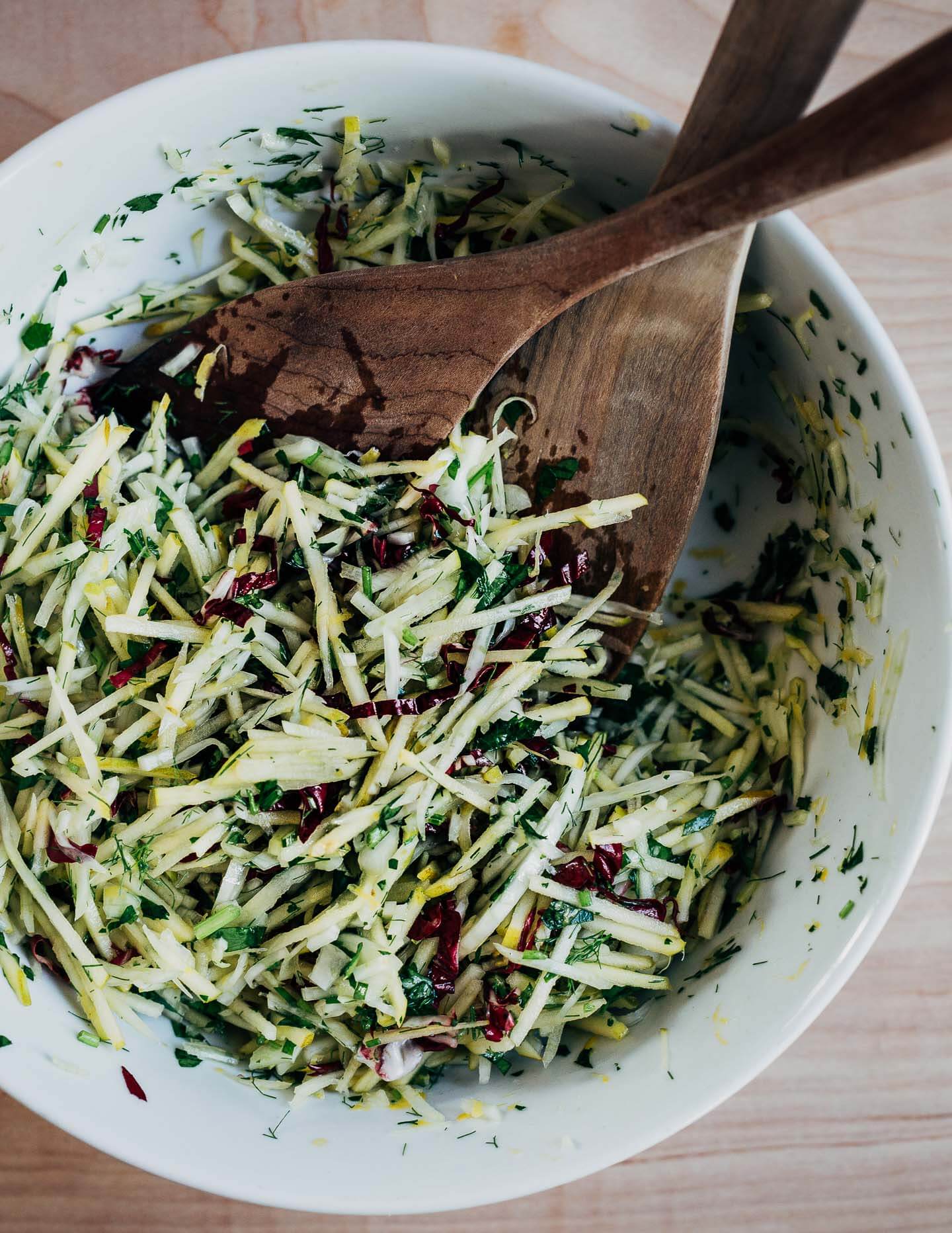 A bowl of slaw with wooden salad tongs.